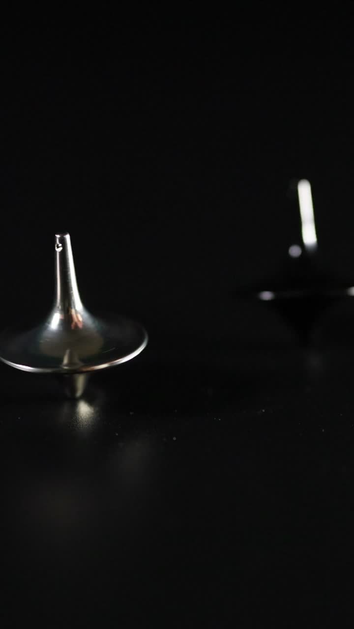 Primi piani di dita che fanno girare diverse trottole metalliche su uno sfondo scuro e minimalista