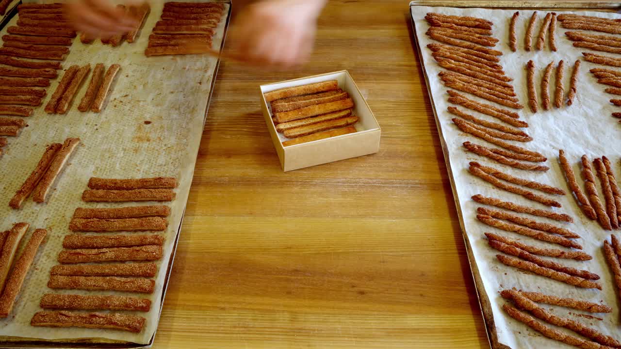 Mani che dispongono bastoncini di cannella su vassoi in una cucina calda e accogliente.