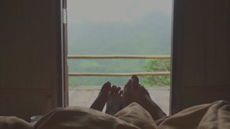 feet of man and woman flirt together from under blanket with the balcony and the mountain landscape background