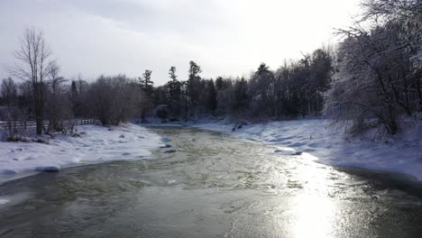 Escena-De-Invierno-Con-Hermosa-Nieve-En-Los-árboles-Antena-Baja-A-Lo-Largo-Del-Río-Medio-Congelado