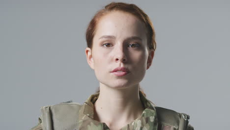 studio portrait of serious young female soldier in military uniform against plain background