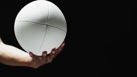 hand of african american man holding white rugby ball on black background, copy space, slow motion