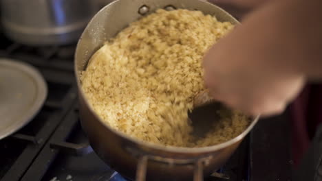 reviro is stirred with a wooden spoon while cooking on a stove, showing golden crumbs forming in the metal pan — traditional rural south american preparation captured in kitchen close-up.