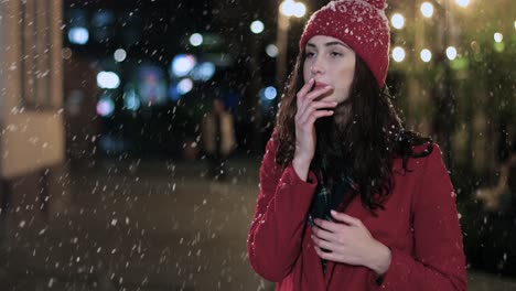 vista cercana de una mujer caucásica enferma con abrigo rojo al aire libre estornudando en la calle mientras nieva en navidad