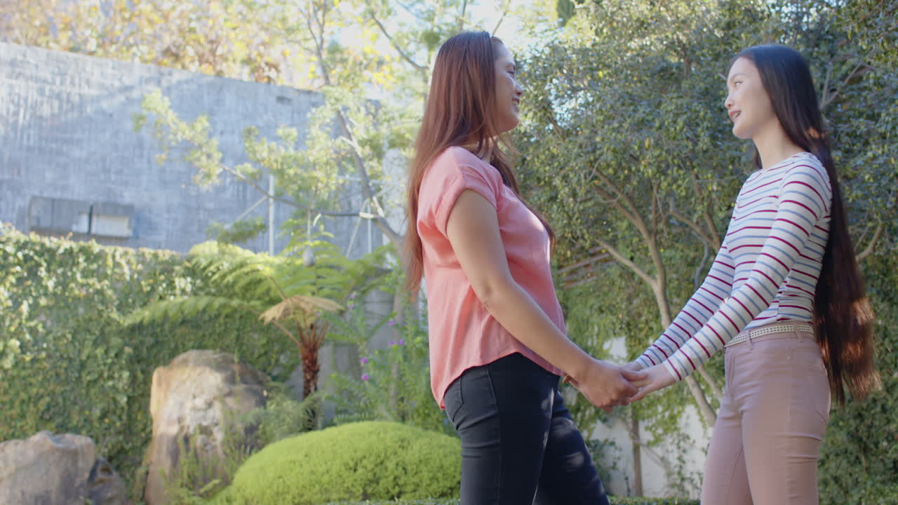 Holding hands, asian mother and daughter smiling and enjoying time together outdoors
