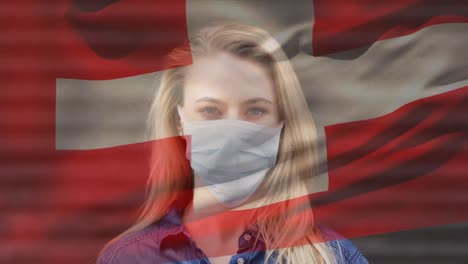 animation of flag of switzerland waving over woman wearing face mask during covid 19 pandemic