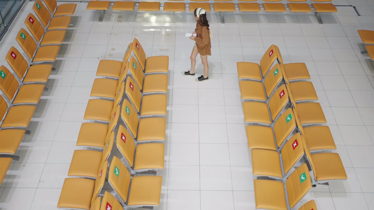 4K Asian woman using mobile phone while waiting for flight at boarding gate in airport terminal.