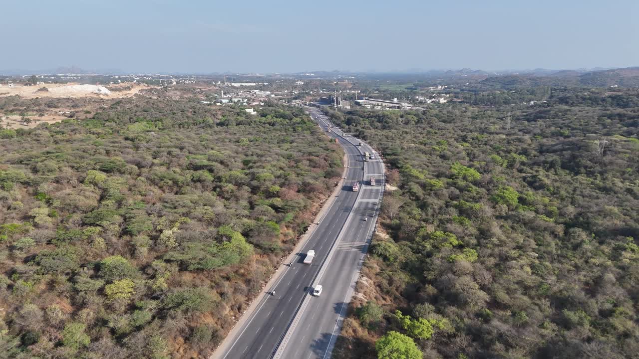 Highway, industry, and natural landscape from above. Traffic flows past factories and green hills under a bright sky. Documentaries on industrial development, infrastructure, or economic growth