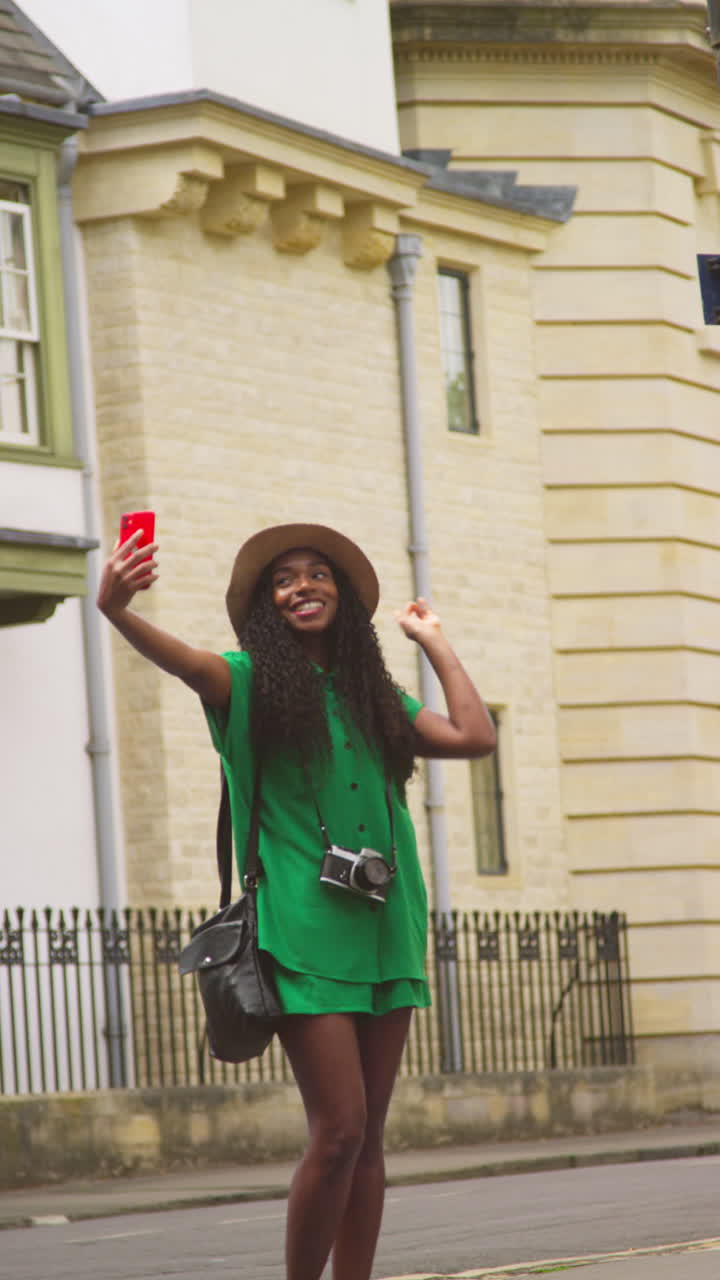 Vertical Video Of Female Tourist On Vacation In Oxford UK Exploring City Walking Along Holywell Street Posing For Selfie On Mobile Phone