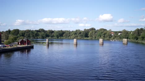 a quiet swedish lake with large concrete bridge supports standing in the water, but no bridge above. a red cabin sits on a dock nearby. a peaceful, atmospheric scene.