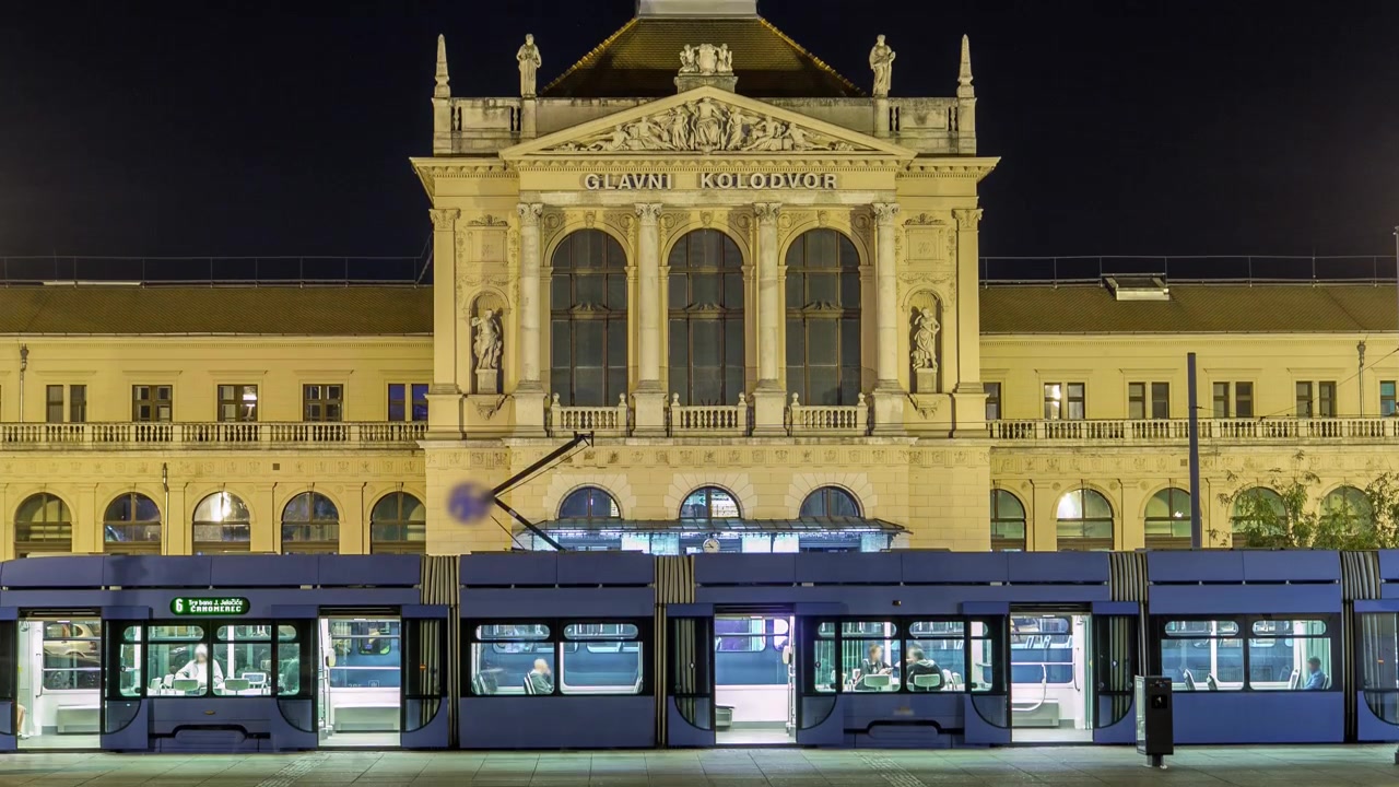 Timelapse notturno di persone in Piazza Tomislav davanti alla Stazione Ferroviaria Centrale, principale snodo della rete ferroviaria croata. Traffico sulla strada. ZAGABRIA, CROAZIA.