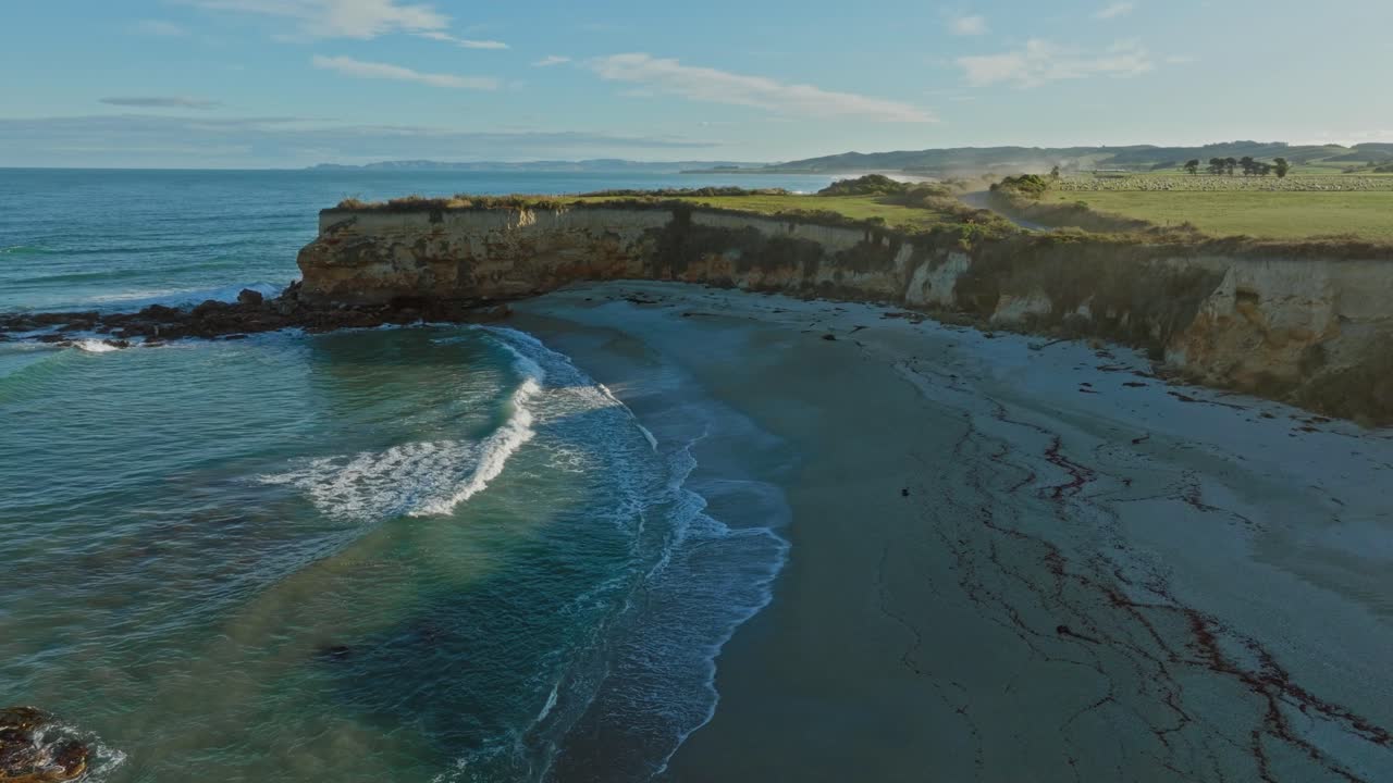 Beautiful aerial view of Mitchells Rocks with secluded, sandy beach, crumbling coastal cliffs and ocean spray over coastal landscape in Otago, South Island of New Zealand Aotearoa