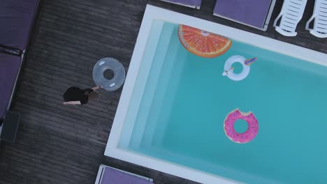 a top view of the pool with multicolored inflatable circles and sun chairses standing by the pool. shooting from the drone.