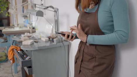 woman craftsperson using smartphone in jewelry workshop