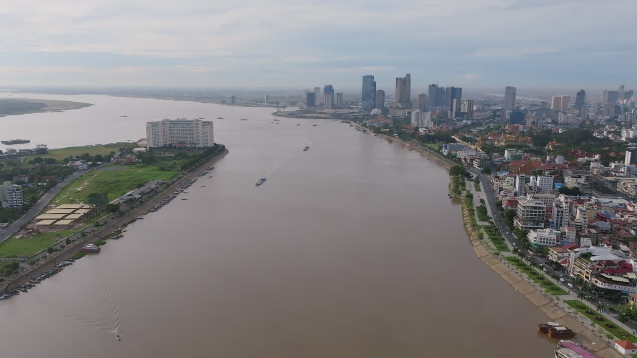Wide aerial of Phnom Penh’s riverside skyline with boats on the water and a large hotel on the peninsula