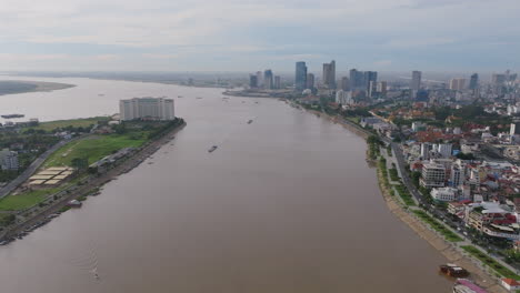 wide aerial of phnom penh’s riverside skyline with boats on the water and a large hotel on the peninsula