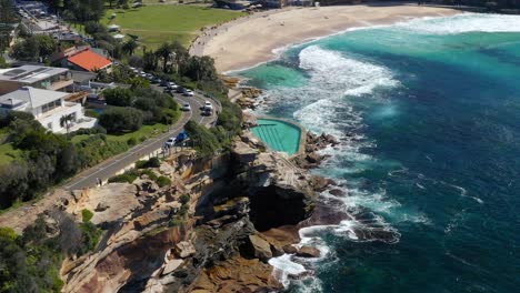 drone hacia la piscina oceánica de bronte con olas chocando contra la costa rocosa en la playa de bronte, nueva gales del sur, australia