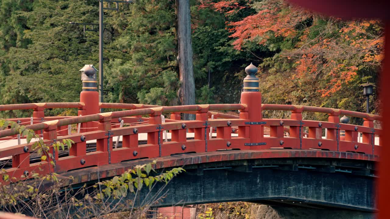 A serene moment of a blonde woman strolling across the iconic Shinkyo Bridge in Nikko, Japan, surrounded by the warm hues of autumn foliage.