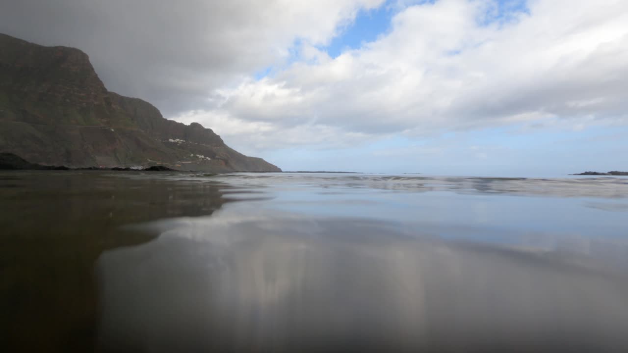 Fredfyldt lavvinkeludsigt over rolige Atlanterhavsvande, der reflekterer dramatiske vulkanske klipper under en skyet himmel ved La Palma, De Kanariske Øer. Perfekt til rejse- og naturprojekter.