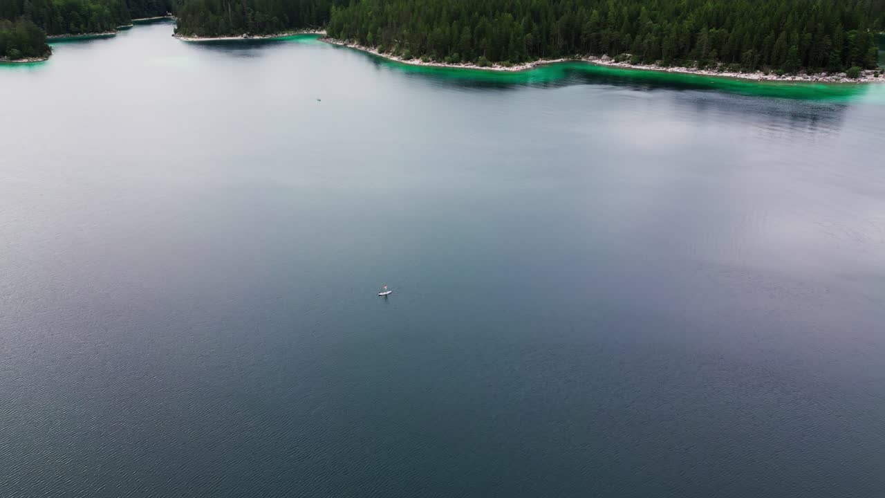 Aerial view of Eibsee lake, a large body of water with an expanse of green pine trees and Germany's highest mountain, Zugspitze in the background