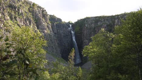 Gran-Tiro-Largo-De-La-Cascada-Njupeskär,-Sumergiendo-Agua-Dulce-Entre-El-Cañón-Erosionado,-En-El-Parque-Nacional-Fulufjället,-Rodeado-De-Abetos-Envueltos-En-La-Luz-Del-Sol,-En-Särna,-Suecia