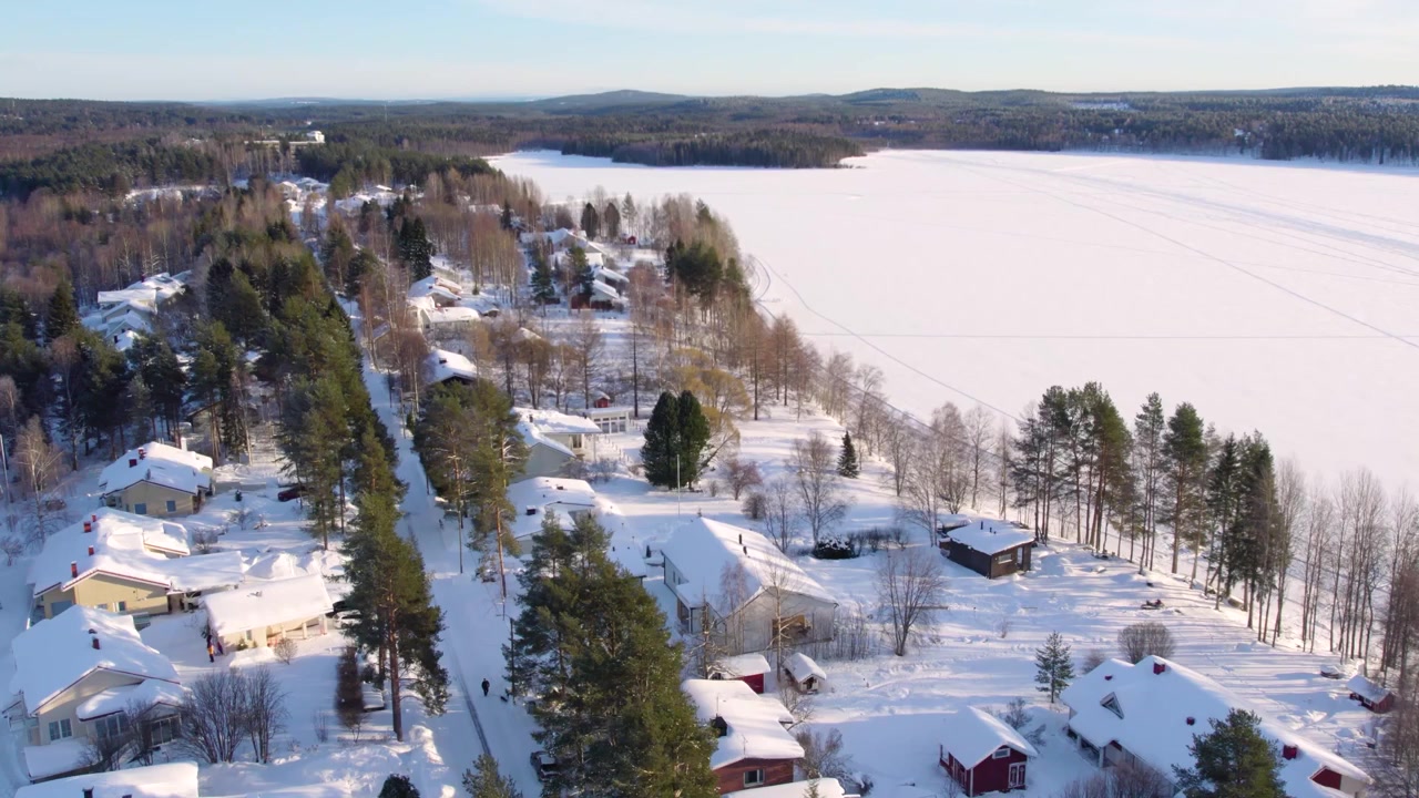 Luftaufnahmen mit Drohne von einem verschneiten Vorort in Rovaniemi, Finnland, die über eine ruhige Winterlandschaft schwenken, umrahmt von zwei zugefrorenen Seen. Ein atemberaubender Blick auf die arktische Schönheit