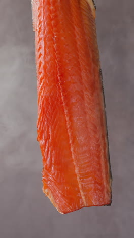 tasty expensive cool smoked chum salmon red fish fillet hangs and turns in floating smoke cloud on light grey background close view slow motion