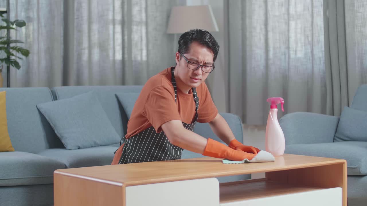 집에서 스프레이로 테이블을 청소하는 동안 등통을 겪는 아프론을 입은 아시아 남성 집사