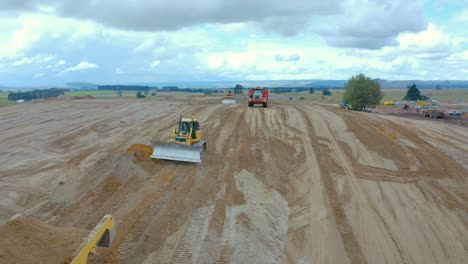 Articulated-dump-truck-dumping-sand-at-development-site-with-bulldozer,-aerial