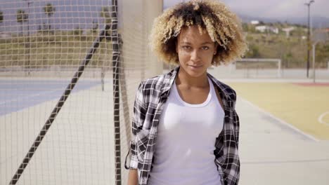 young woman with skateboard poses by ball court