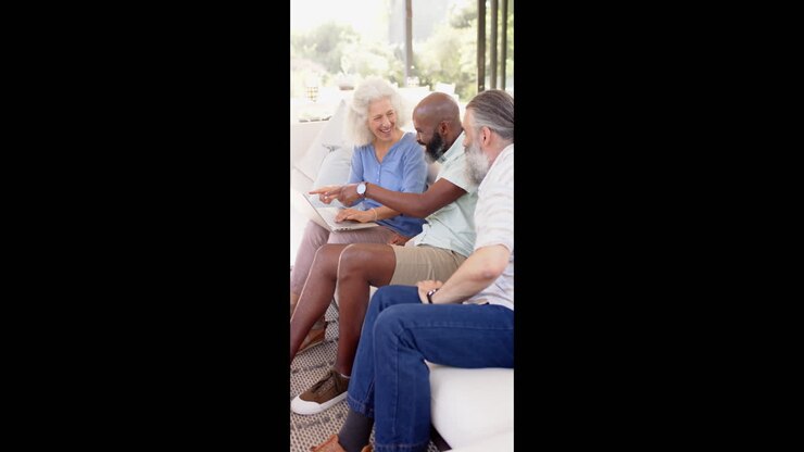 Vertical video: Seniors sitting on couch, using laptop and discussing something together