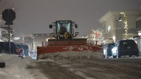 man operating bulldozer at night to clear snow from city street by plowing