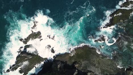 toma aérea estática de las olas del mar del océano índico golpeando rocas y rocas en la playa en condiciones soleadas clima - pengilon hill, indonesia, asia