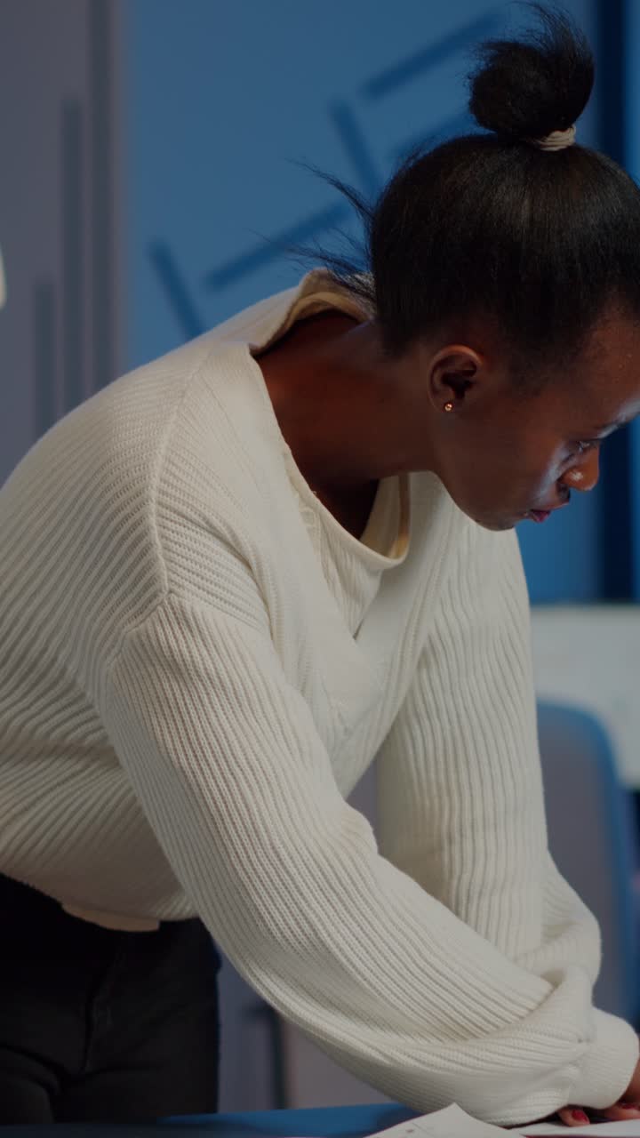 Vertical video Stressed african manager woman reading raports, standing at desk