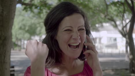 Cheerful-mature-lady-talking-on-smartphone-in-summer-park