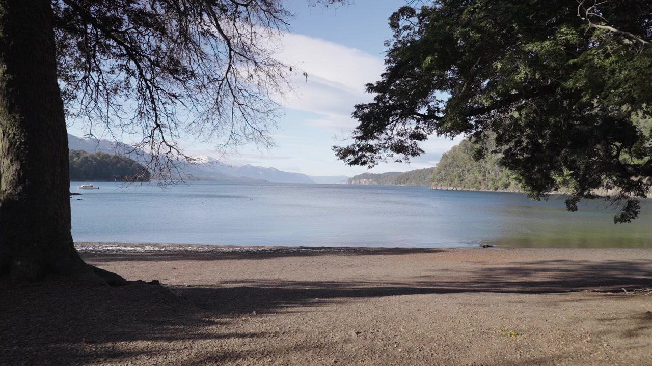 Una tranquilla scena lacustre con alberi che incorniciano la vista della Baia Mansa sotto un cielo sereno. Ideale per contenuti di viaggio e documentari sulla natura