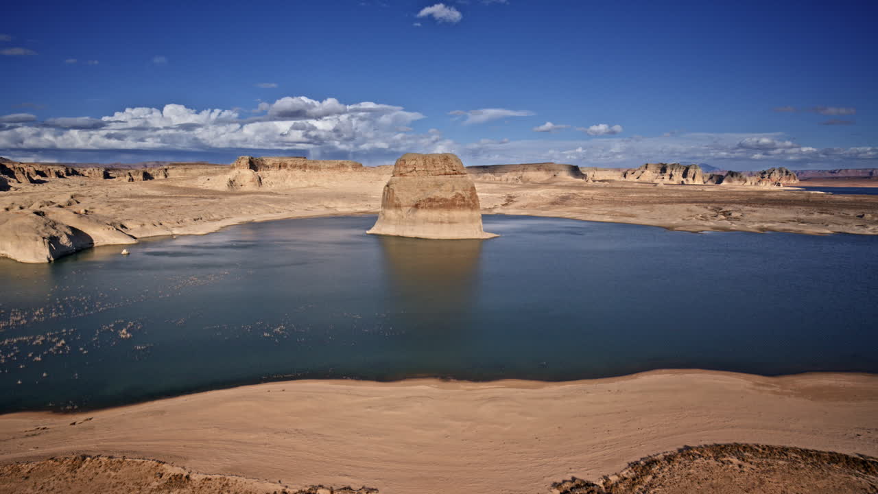 Drone shot showing massive lone rock in lake powell framed by a desert canyon landscape near Page Arizona