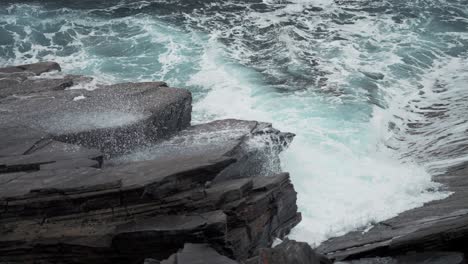 heavy waves hit the dark jagged rocks on the shoreline