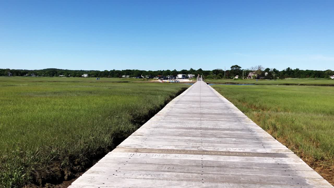 Camera tilt of lonely boardwalk in nature with lush green grass near Town Neck Beach of Sandwich Massachuetts New England USA