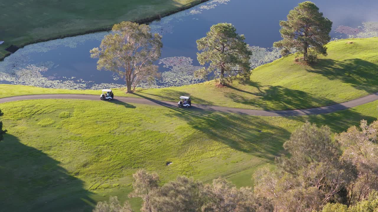 Golf carts traverse a scenic course at sunset, surrounded by lush greenery and tranquil water, creating a serene atmosphere