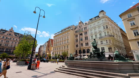 vienna, austria - june 9, 2025: beautiful square with a fountain in the middle. multiple pedestrians walk by the old town of vienna, austria