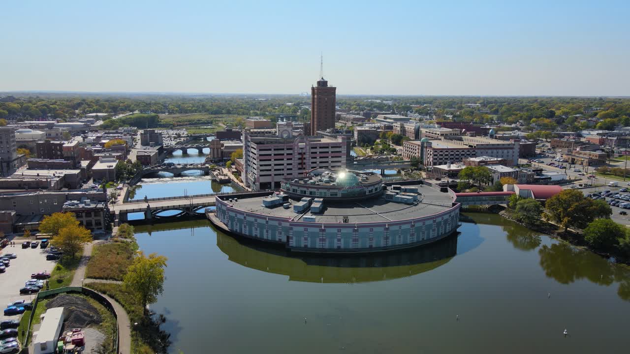 Drone footage capturing downtown Aurora, IL, a Chicago suburb in the Chicagoland area, near the river, buildings, and the Metra train line. Dolly Backward Day S