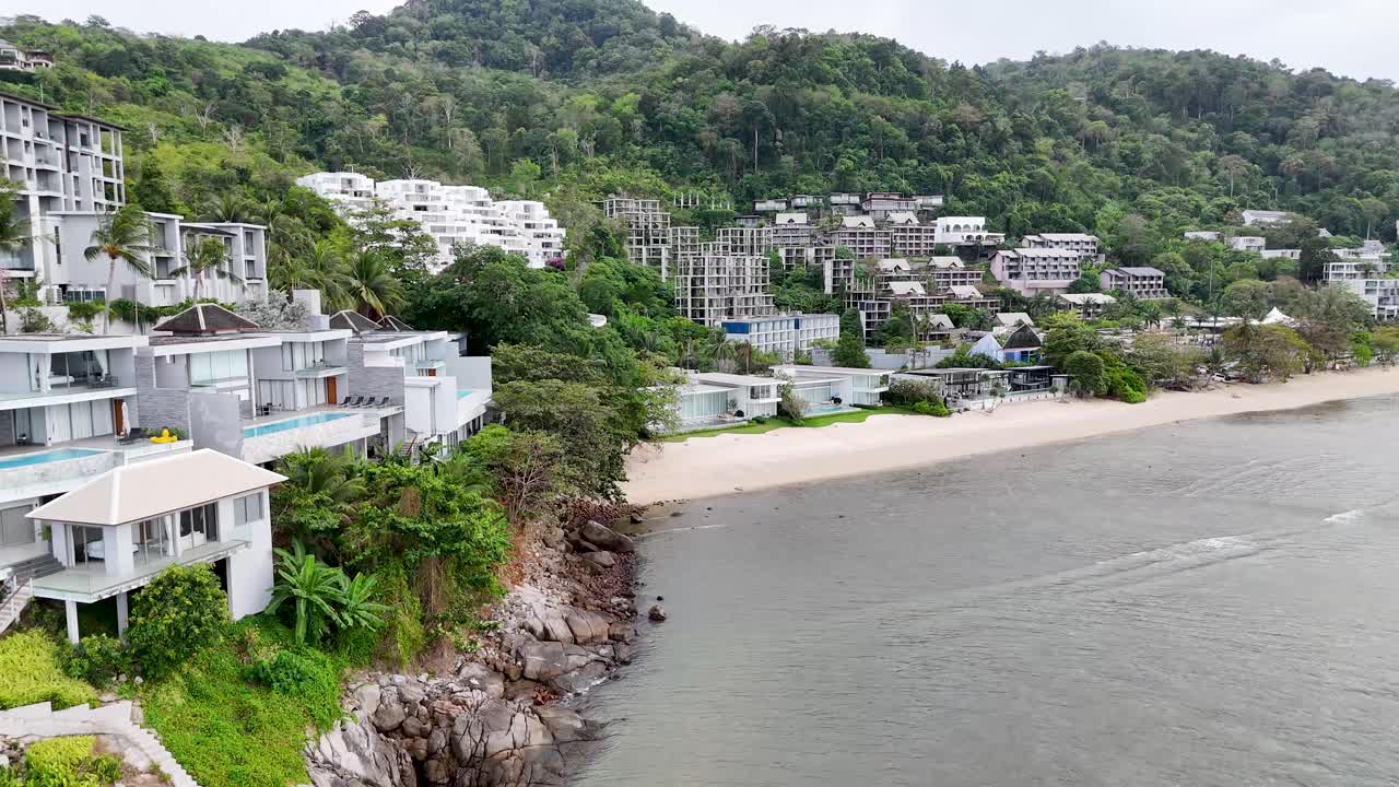 푸켓의 카말라 해변을 따라 고급 빌라의 공중 풍경, 울창한 초록색과 조용한 해안 풍경 속에서 현대적인 건축을 보여줍니다.