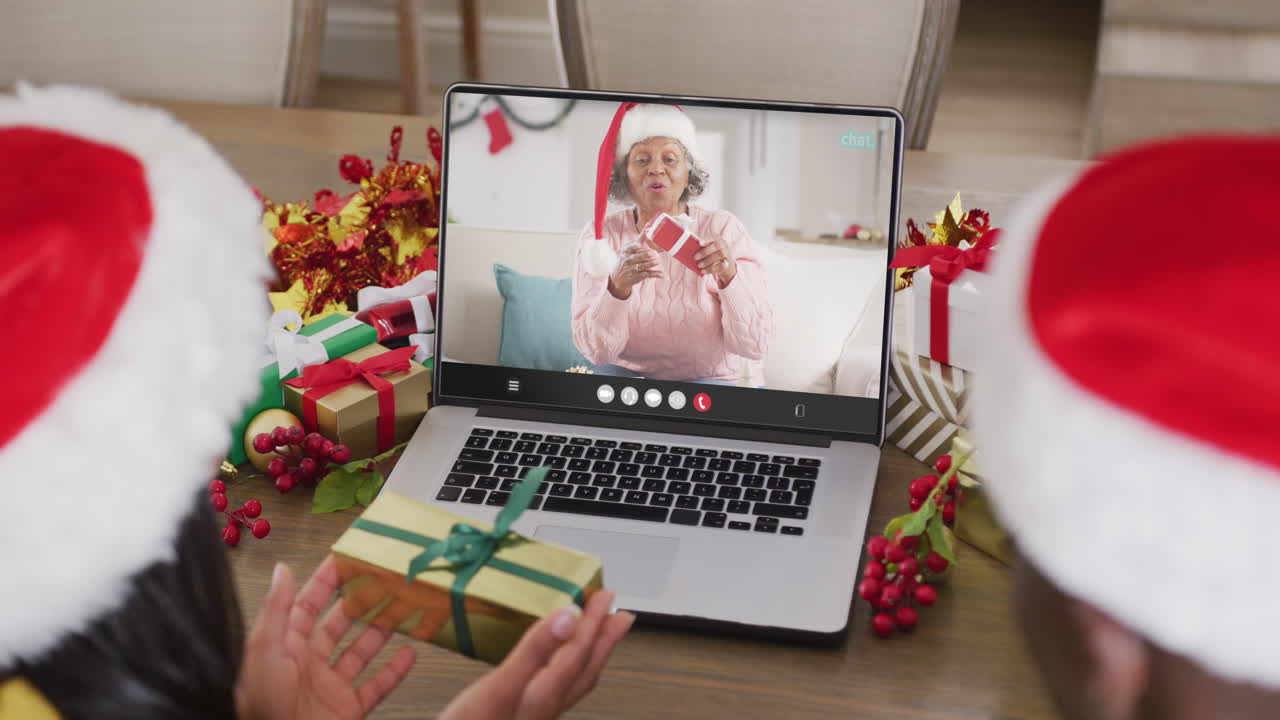 pareja diversa con sombreros de santa teniendo llamada de video portátil con feliz mujer afroamericana