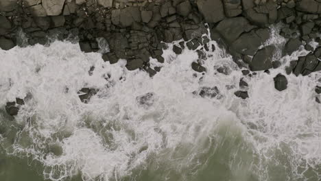 amplias imágenes aéreas en cámara lenta de arriba hacia abajo de las olas del océano chocando contra las rocas