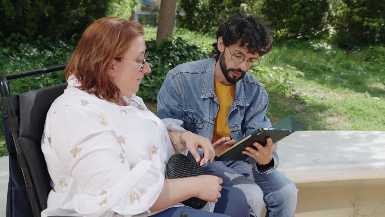 Woman in wheelchair with young man using tablet