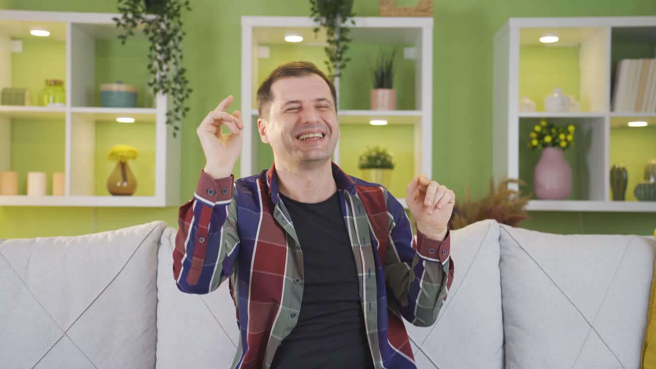 hombre sentado en el sofá en casa bailando feliz de buen humor.