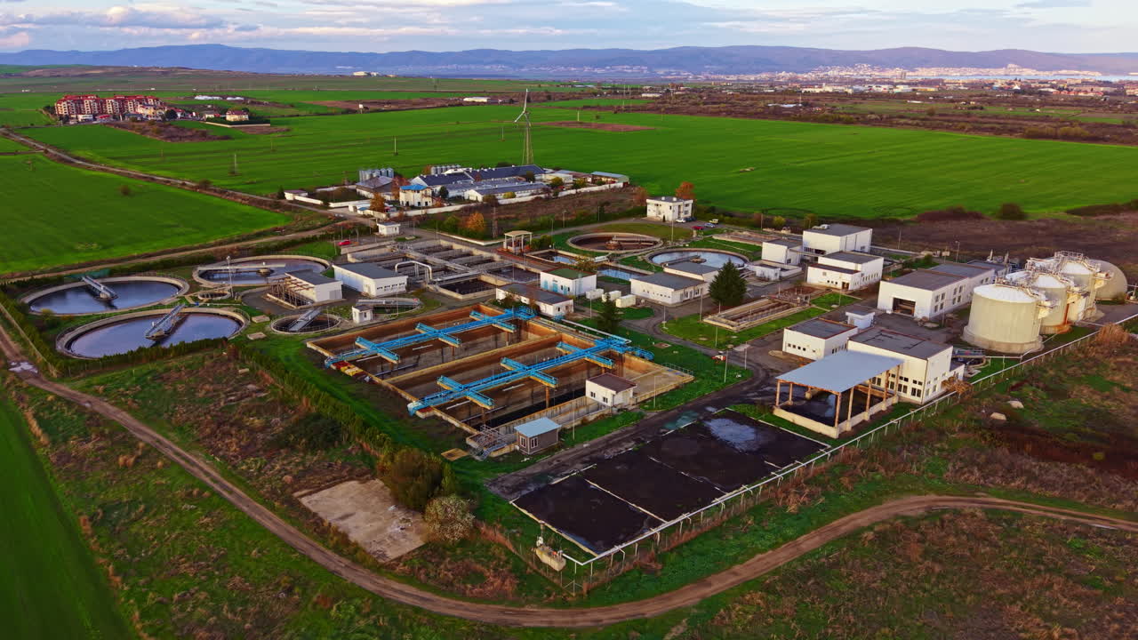 Landscape view of a modern wastewater treatment facility surrounded by green fields and distant mountains during a clear day
