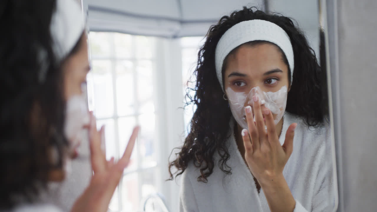 mujer de raza mixta aplicando crema facial en el baño