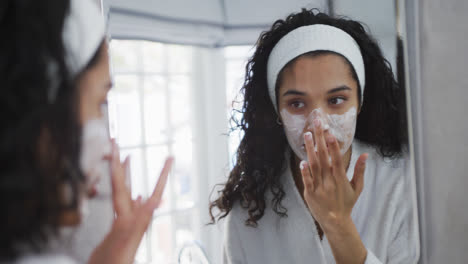 mulher de raça mista a aplicar creme facial na casa de banho.